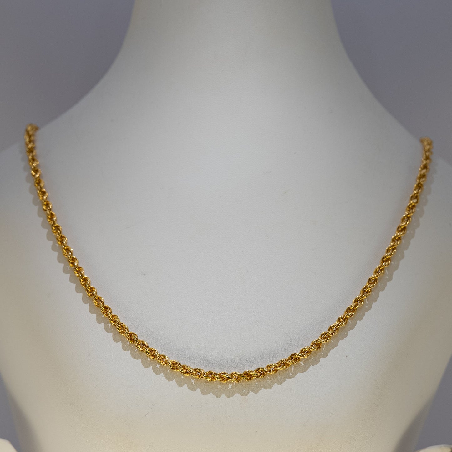 Gold necklace on a mannequin against a gray background
