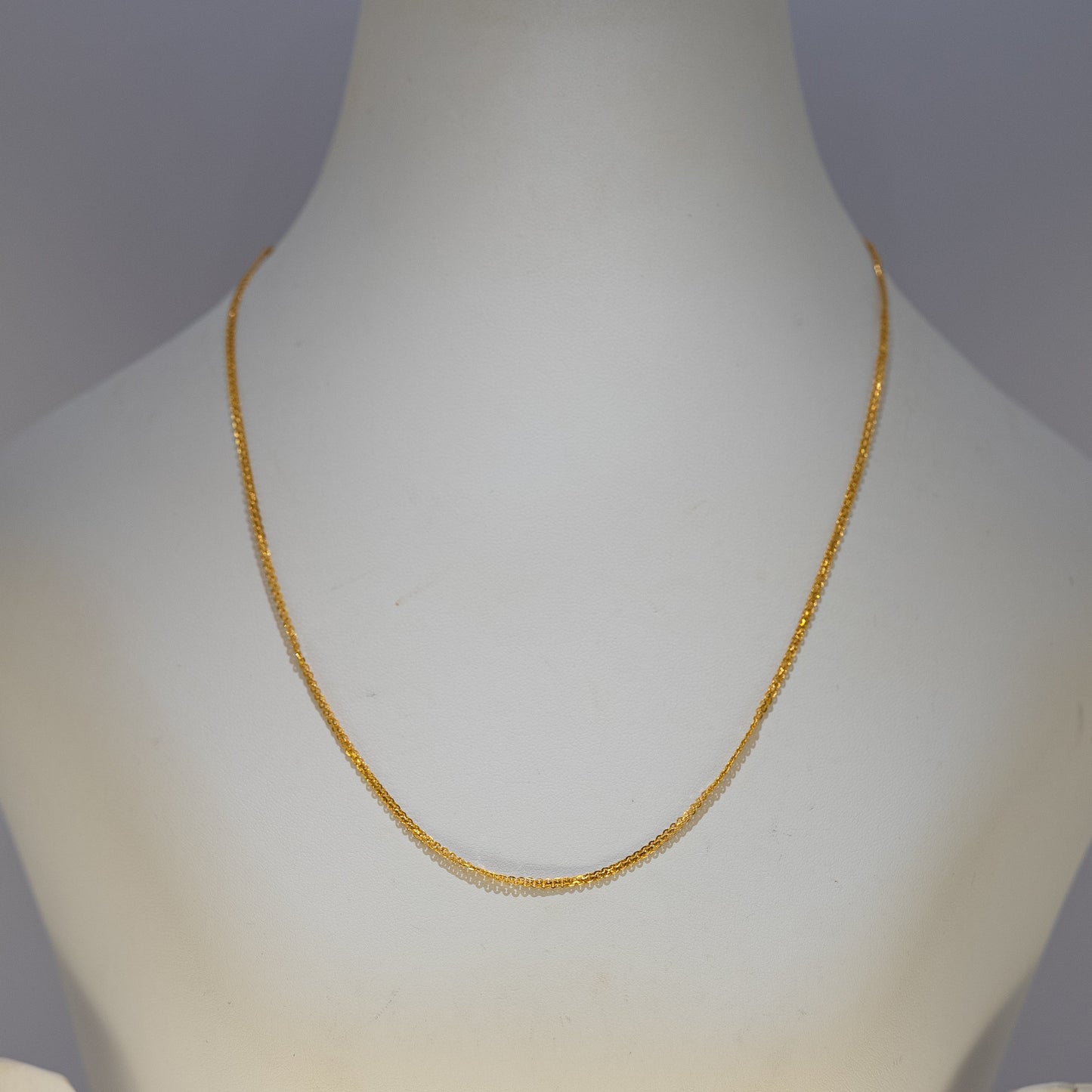 Gold necklace on a mannequin bust against a plain background