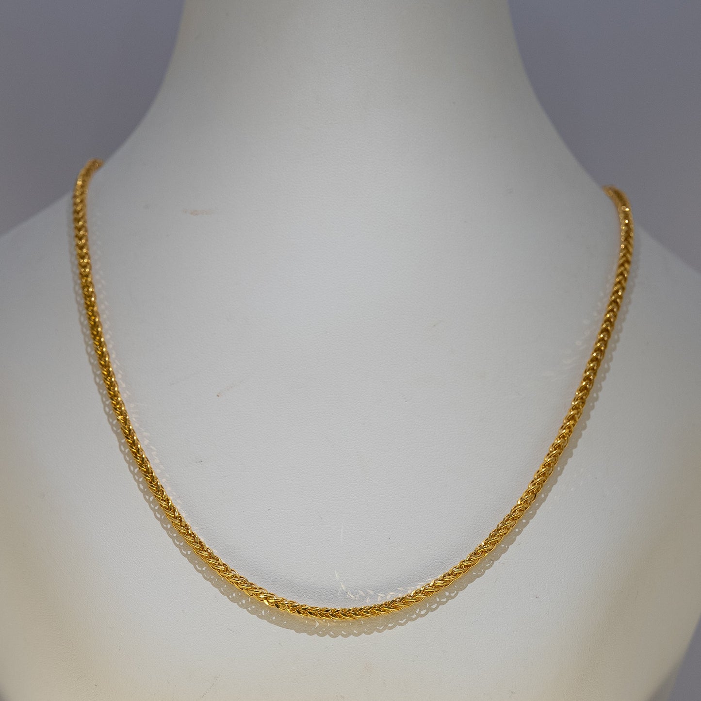 Gold necklace on a mannequin against a gray background
