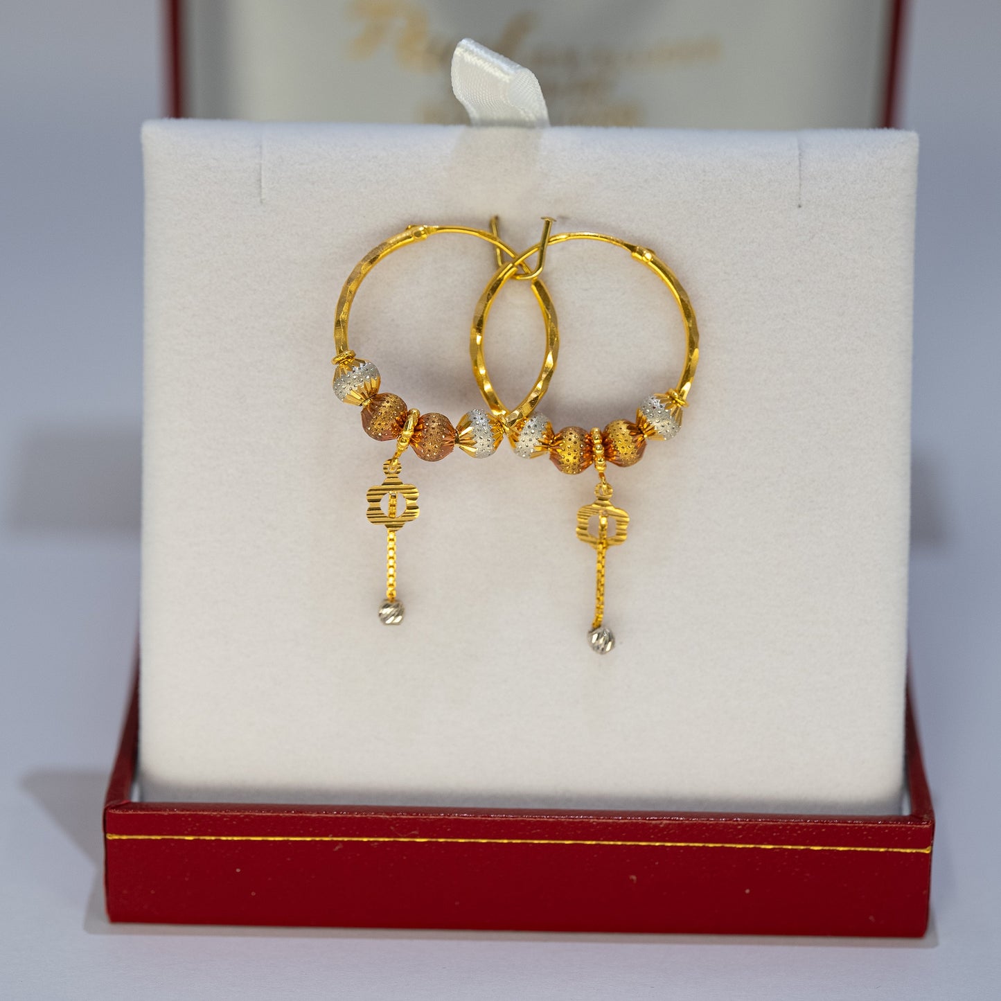 Gold hoop earrings with beads on a white cushion in a red jewelry box.