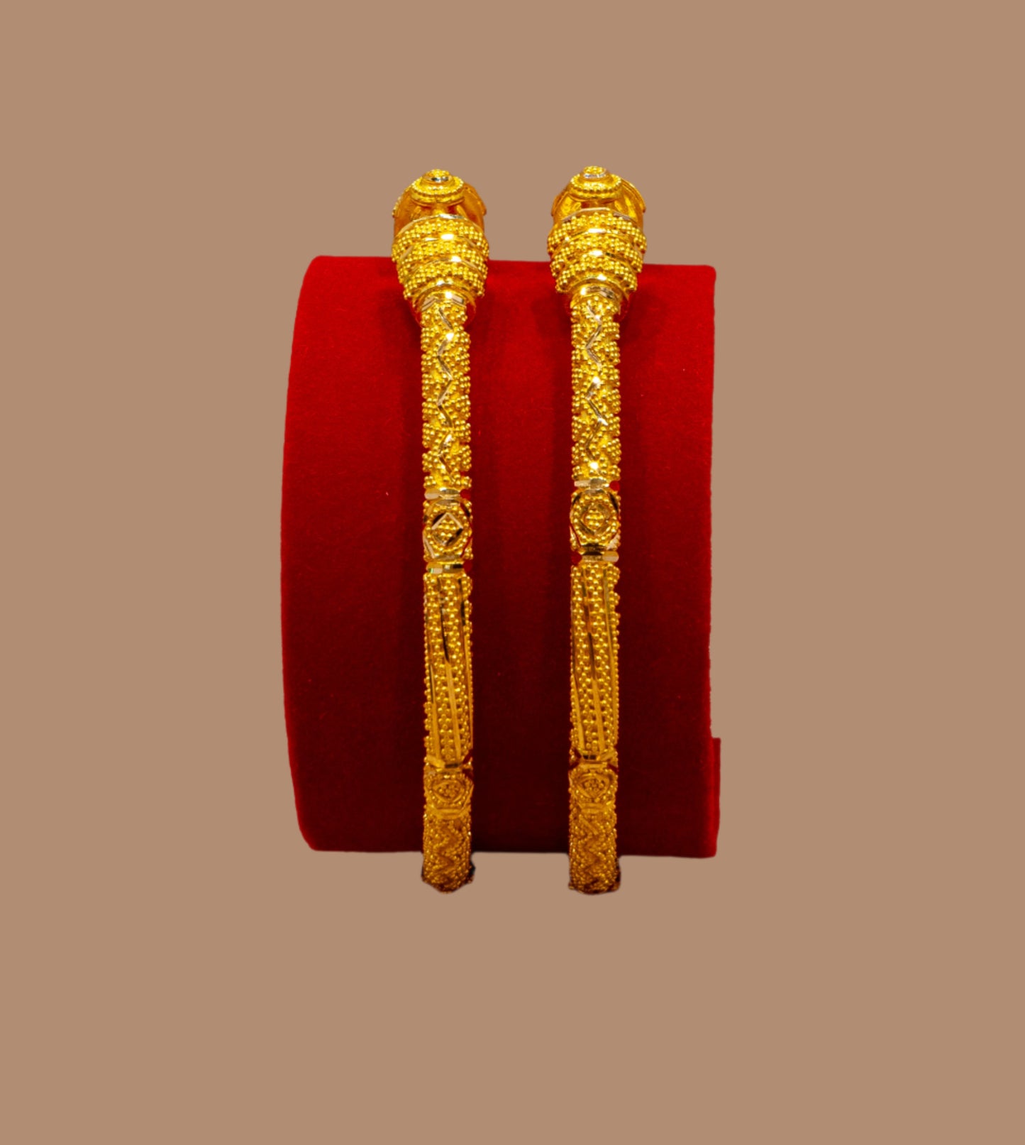 Gold bangles on a red cushion against a beige background