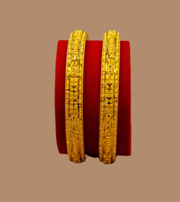 Two gold bangles on a red cushion against a beige background