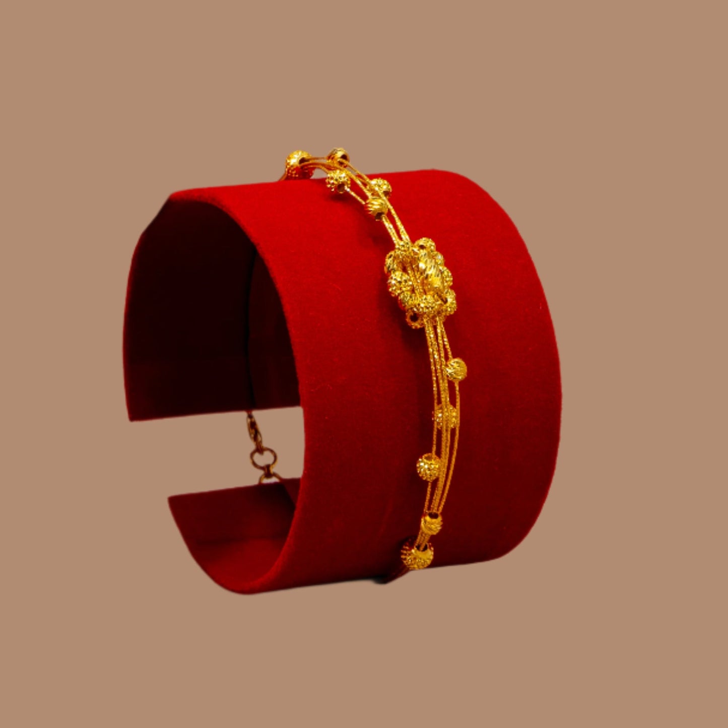 Gold bracelet on a red stand with a hand holding it, against a beige background