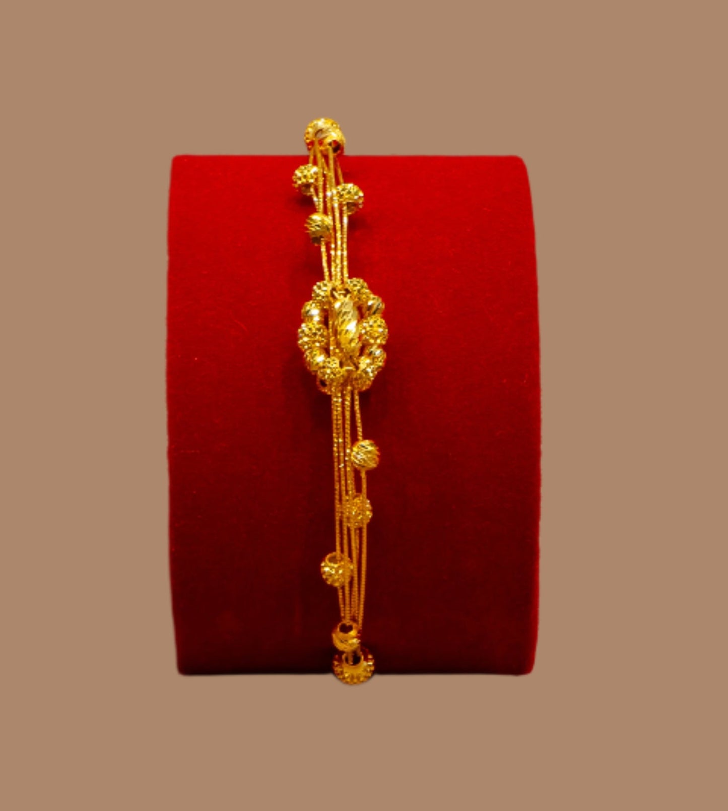Gold bracelet on a red velvet cushion against a beige background