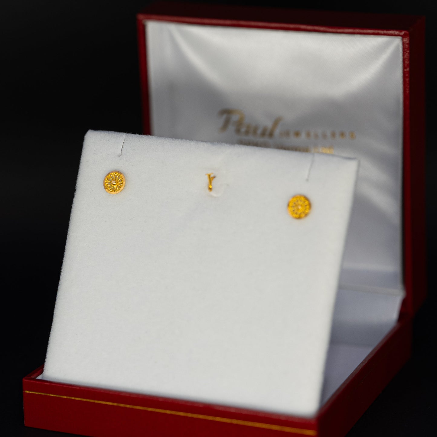 Gold earrings in a jewelry box with a visible brand name.