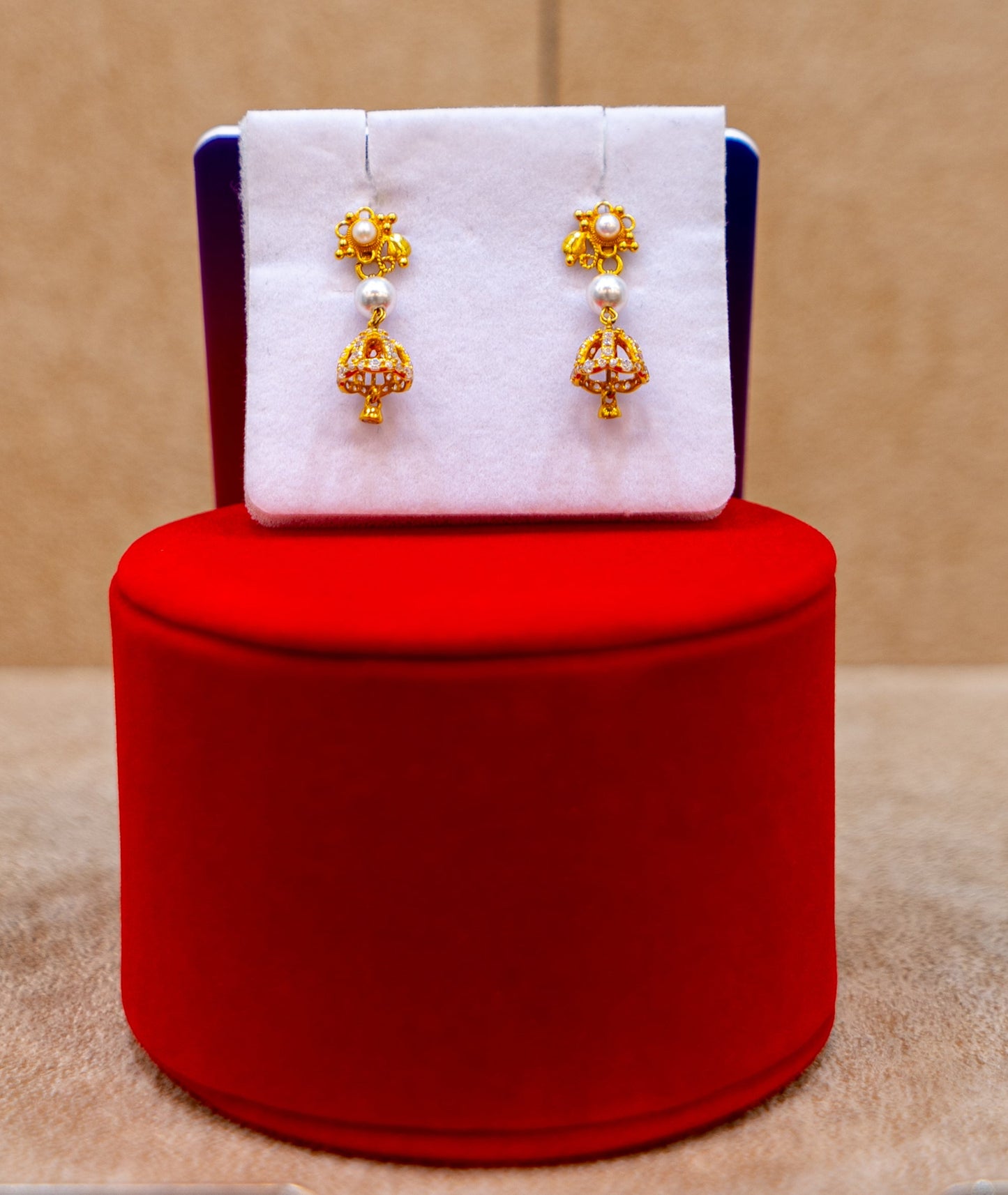 Gold earrings on a white card with a red cushion against a beige background