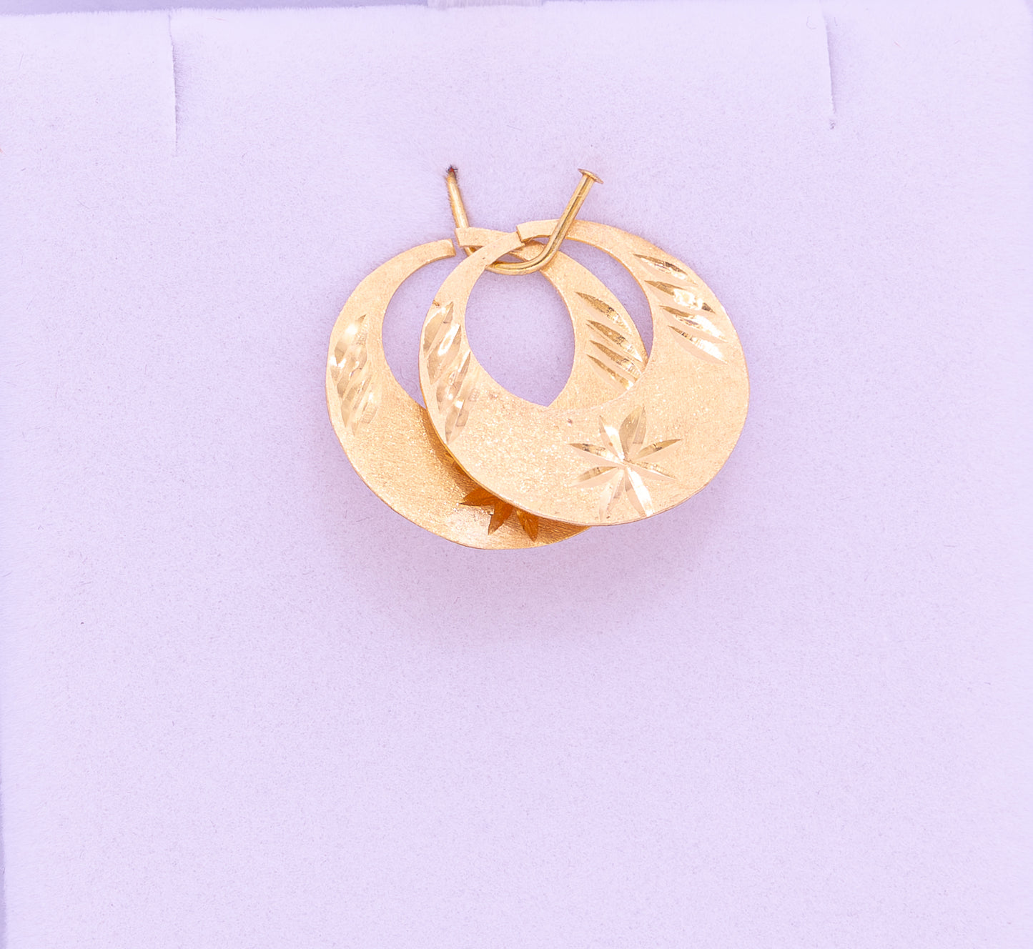 Gold hoop earrings on a light purple background