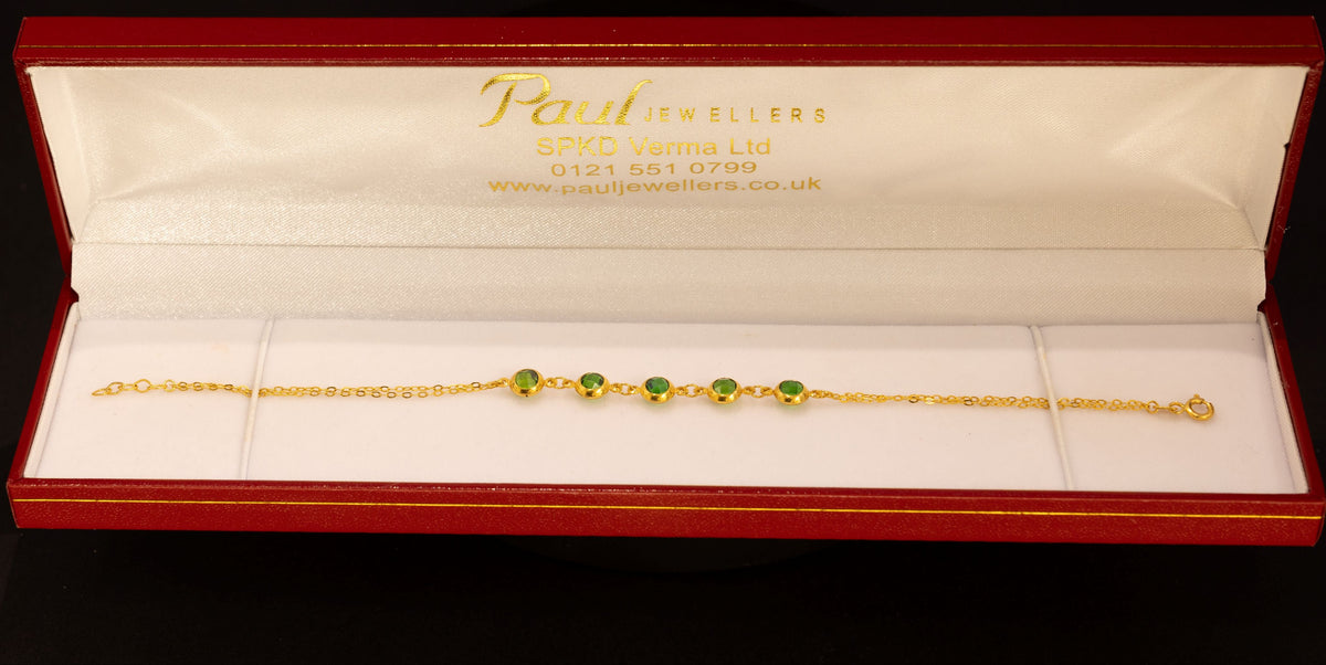 A delicate gold chain bracelet with three small green bead accents, presented inside an open red jewelry box with a white interior. The brand name 'Paul Jewellers' is visible on the inside lid.