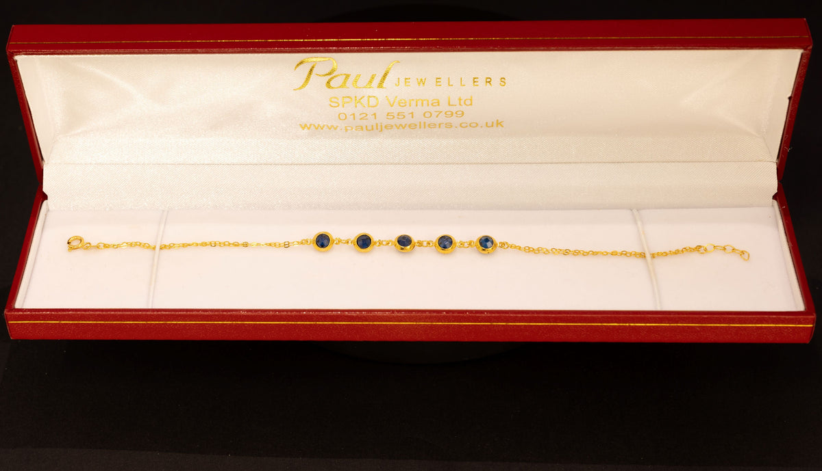 A gold chain bracelet with four dark green oval gemstones, presented in an open red Paul jewelry box on a black background.