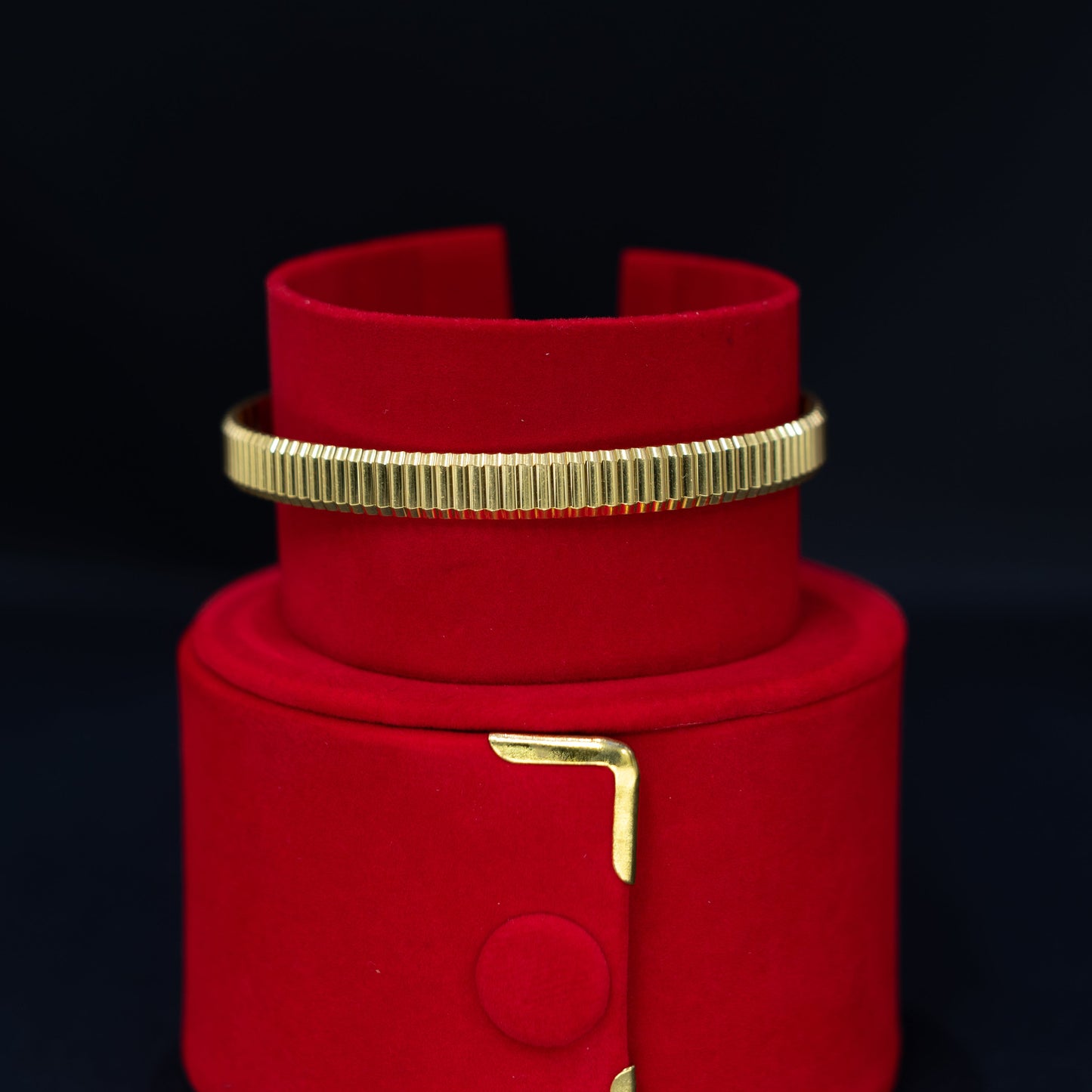 A red velvet jewelry display stand with gold-tone metal accents, holding a matching red cuff bracelet with a ribbed gold band.