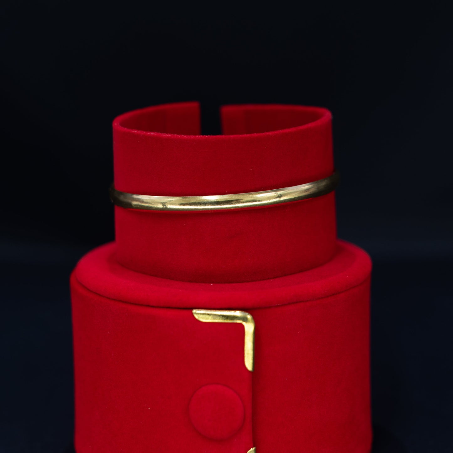 A red velvet jewelry display stand with gold-tone metal accents, including a small ring holder on the upper tier and a decorative bracket on the lower tier, set against a dark background.