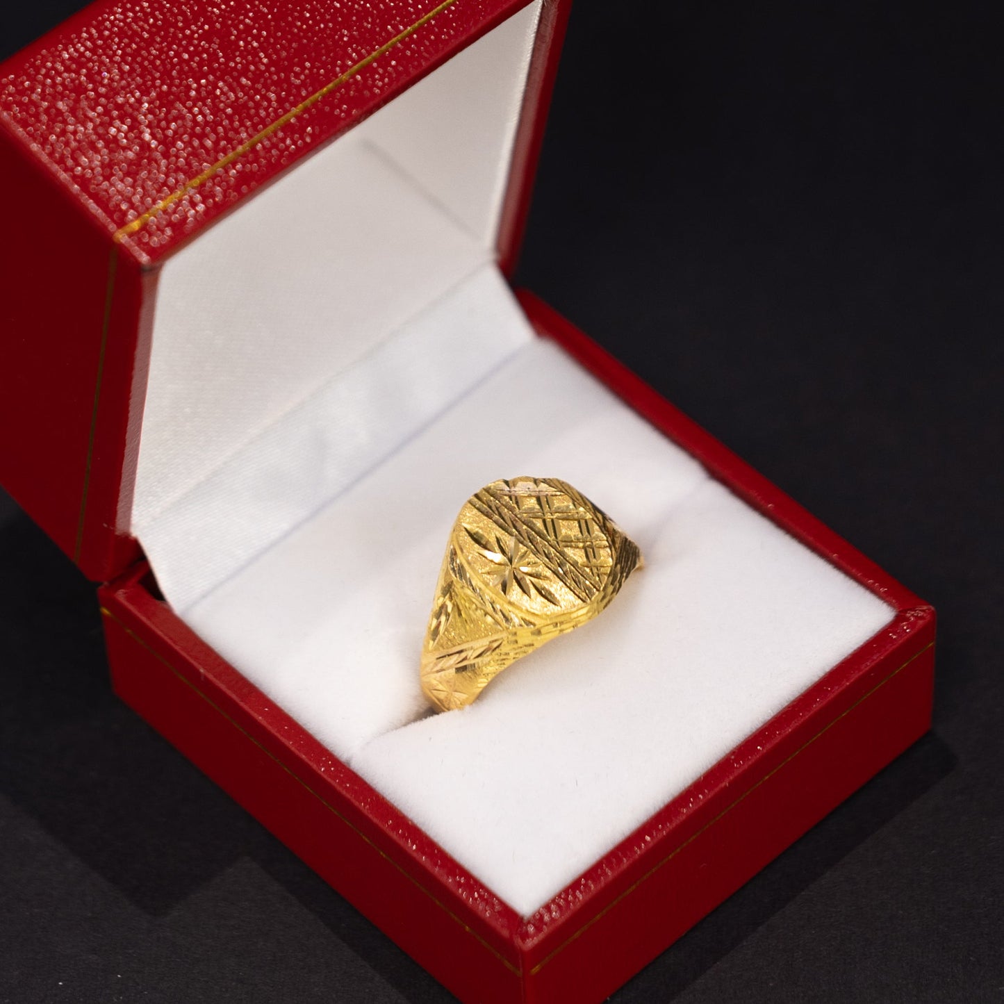 A textured gold ring displayed inside an open red jewelry box with a white cushion, set against a dark background.