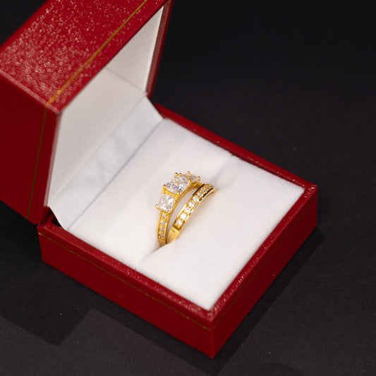 A gold ring with clear gemstones displayed inside an open red jewelry box on a dark background.