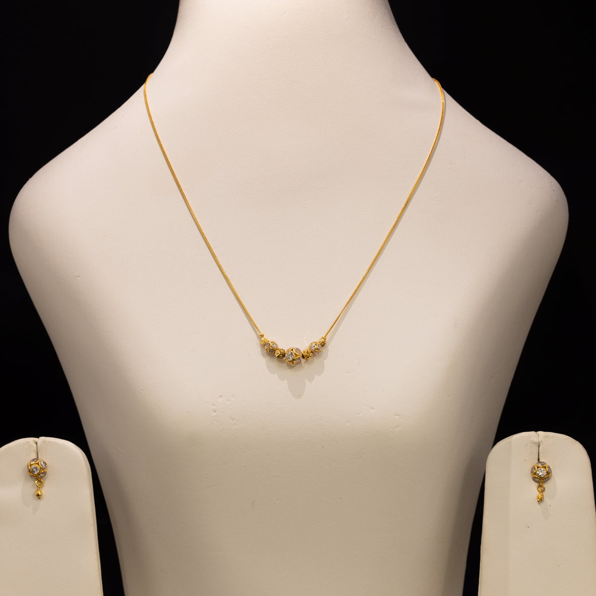 Gold necklace and matching earrings displayed on a white jewelry bust against a black background.