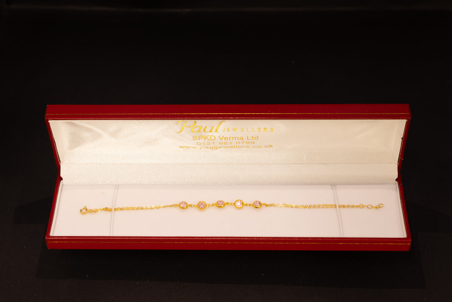 A delicate gold chain bracelet with oval-cut clear stones, presented in an open red Jewellery gift box on a black background.