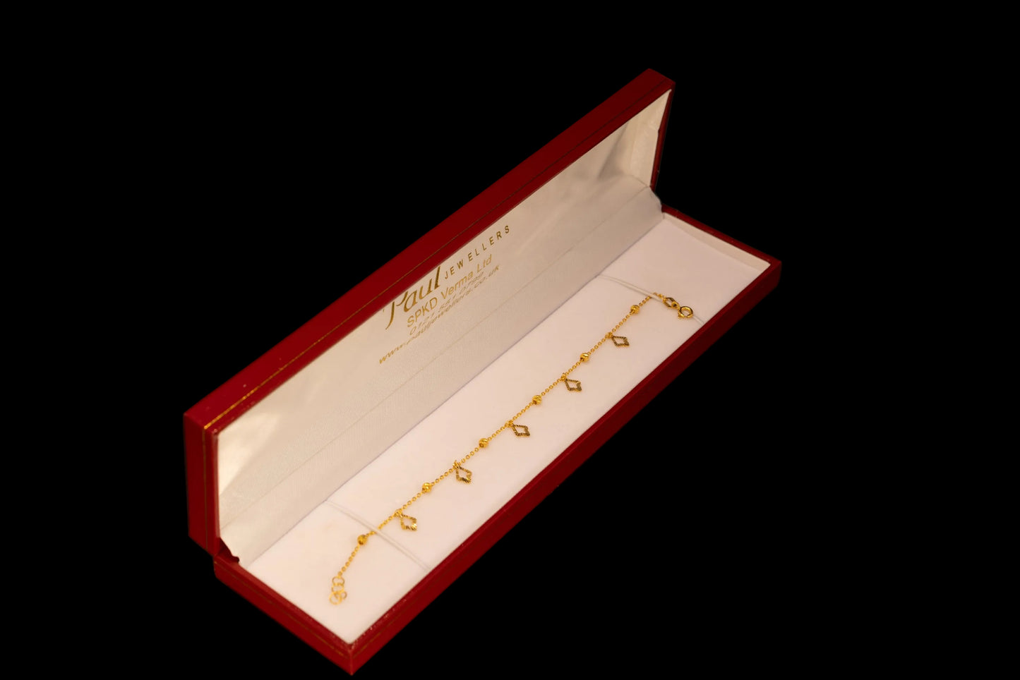 A gold chain bracelet with small diamond-shaped charms, displayed inside an open red and white box on a black background.