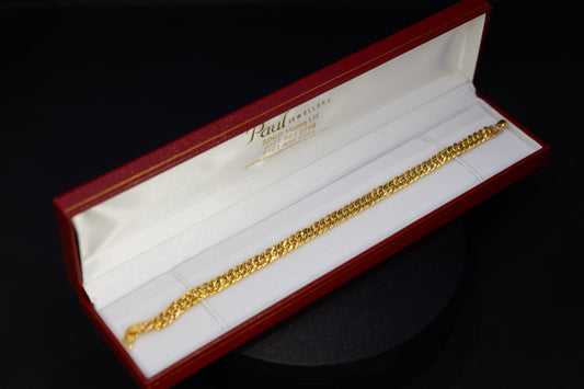 A gold chain bracelet displayed inside an open red and white Audemarsault jewelry box on a black background.