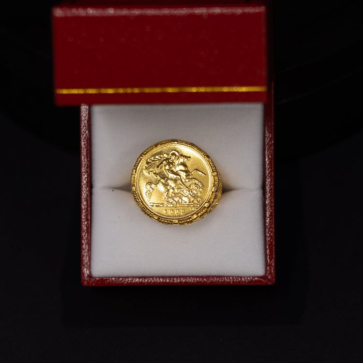A round gold coin or medallion displayed inside an open red jewelry box with a white insert, set against a black background.