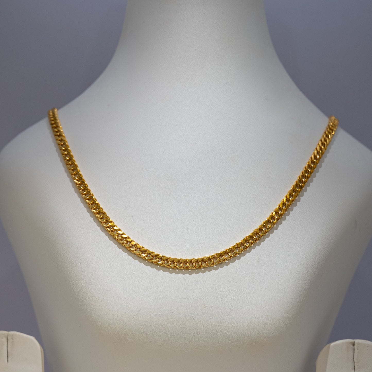 Gold chain necklace on a mannequin bust against a gray background