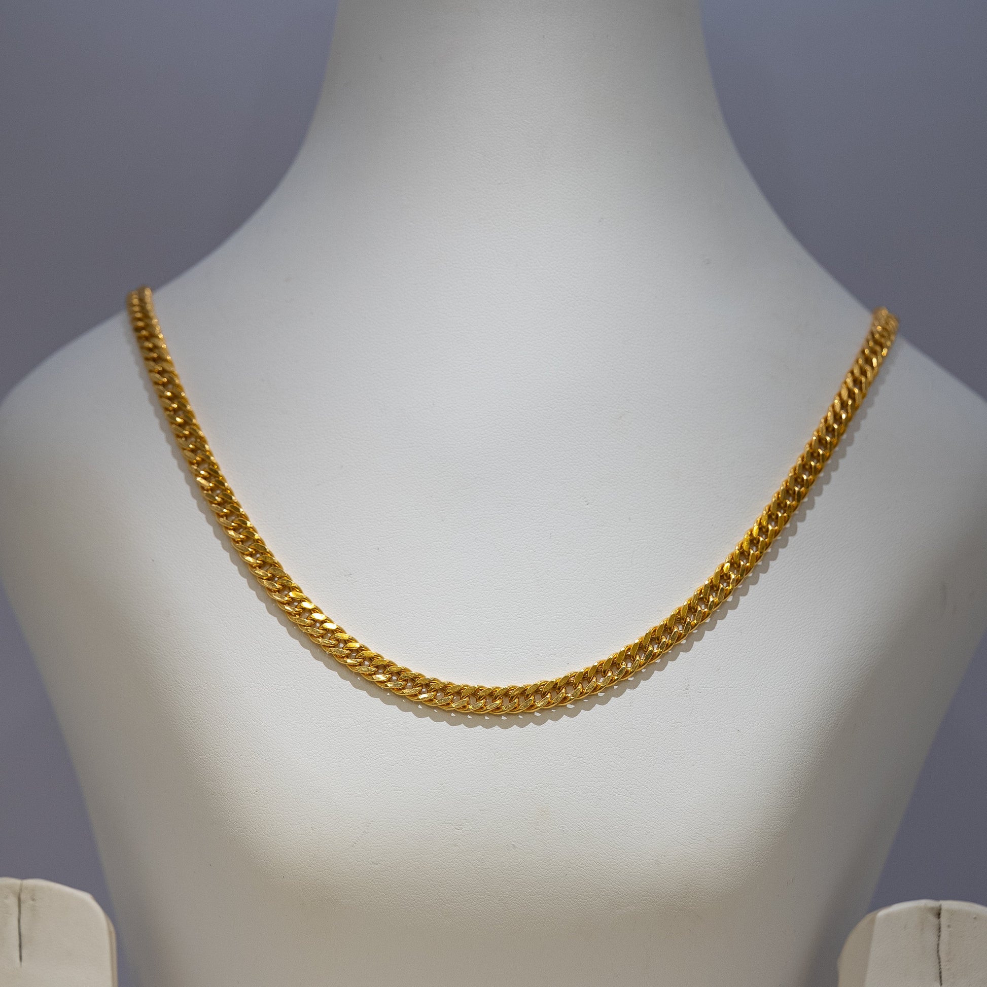 Gold chain necklace on a mannequin bust against a gray background