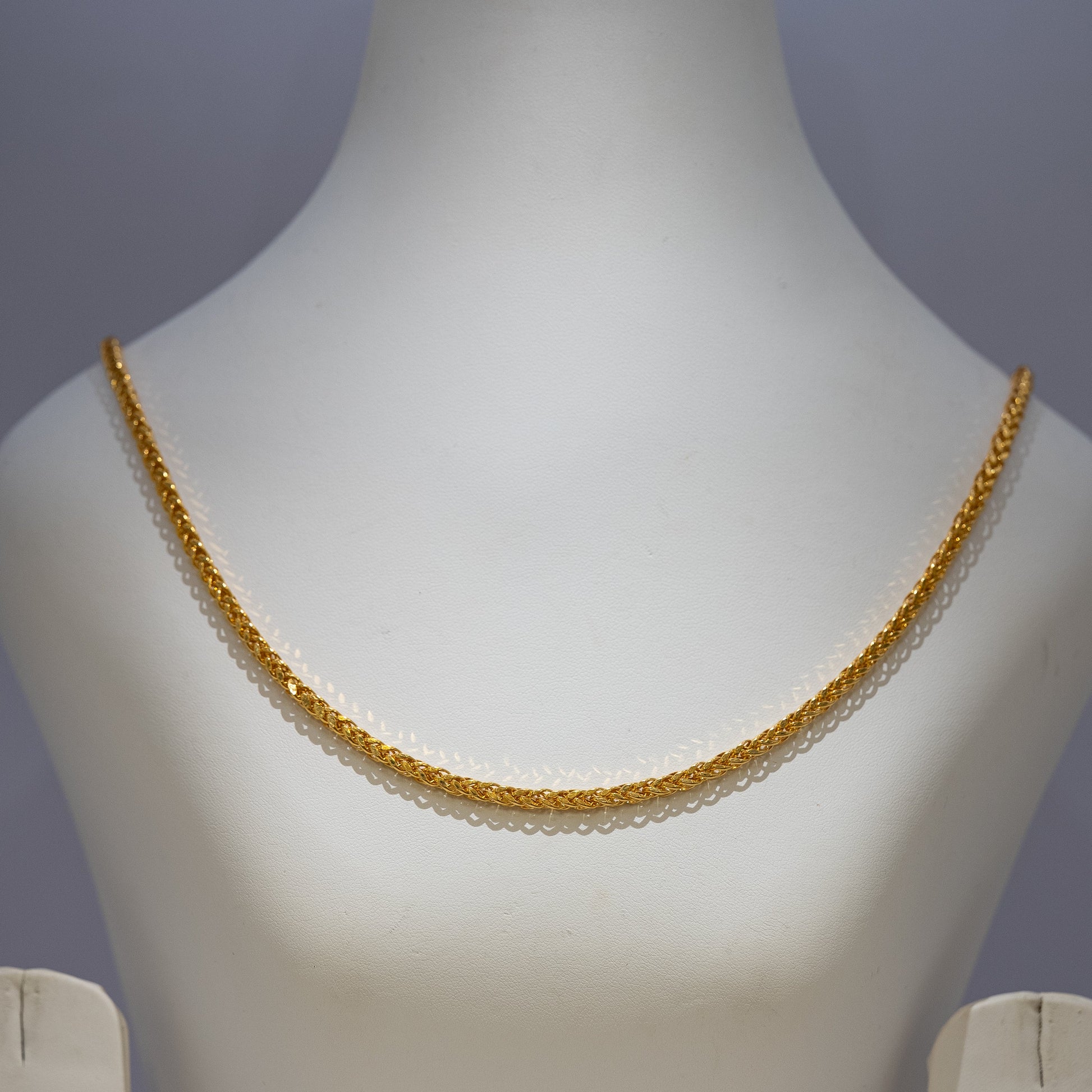 Gold necklace on a mannequin against a gray background