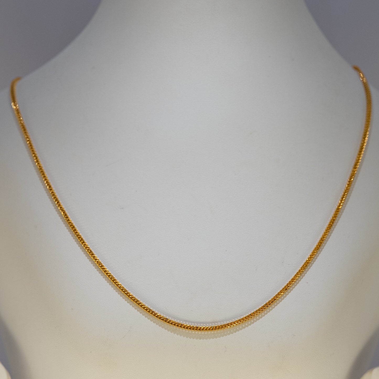Gold necklace on a mannequin against a gray background