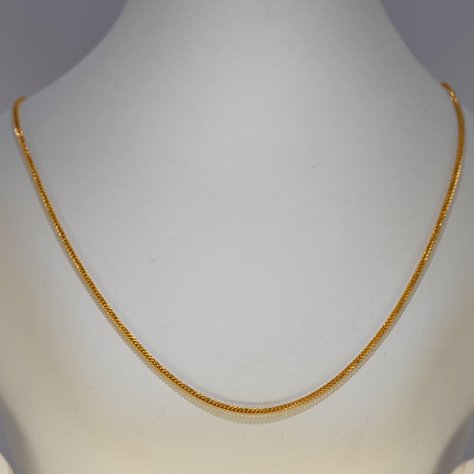Gold necklace on a mannequin against a gray background
