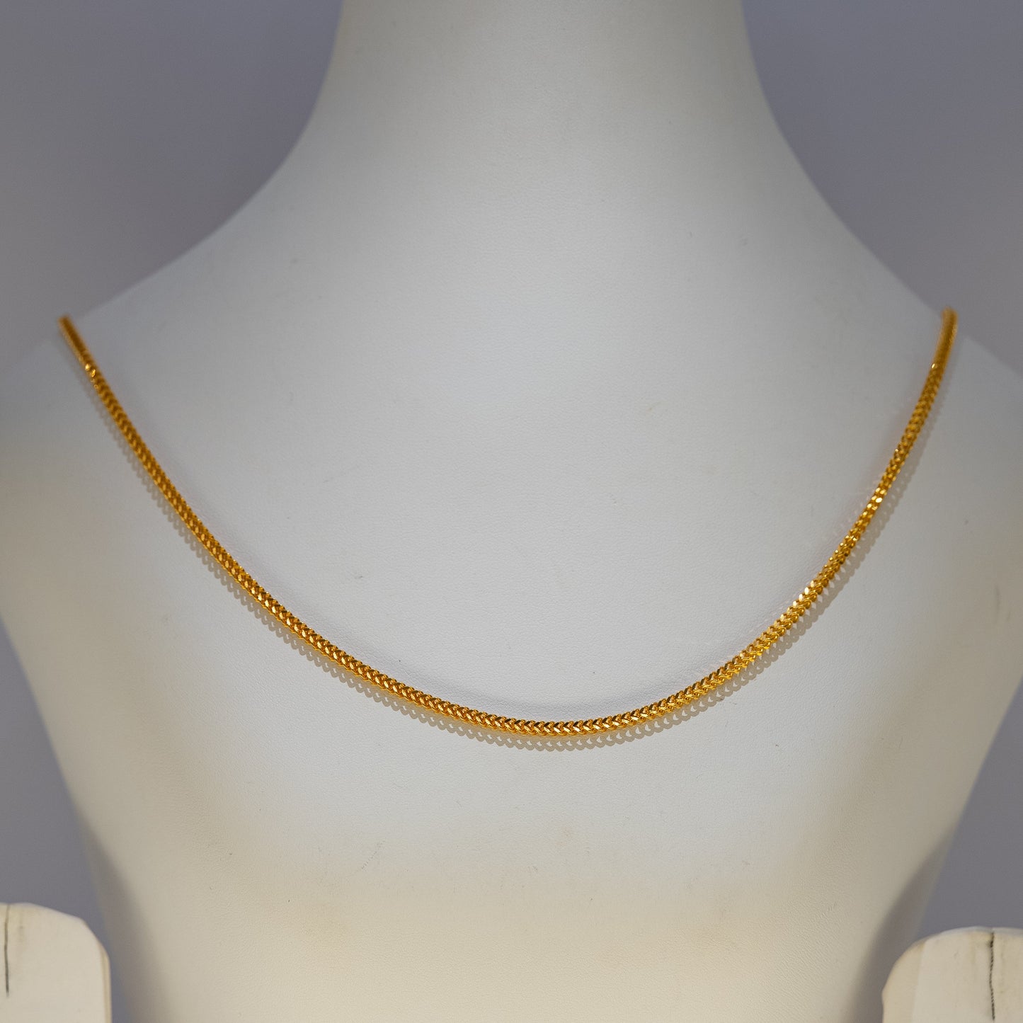 Gold necklace on a mannequin against a gray background