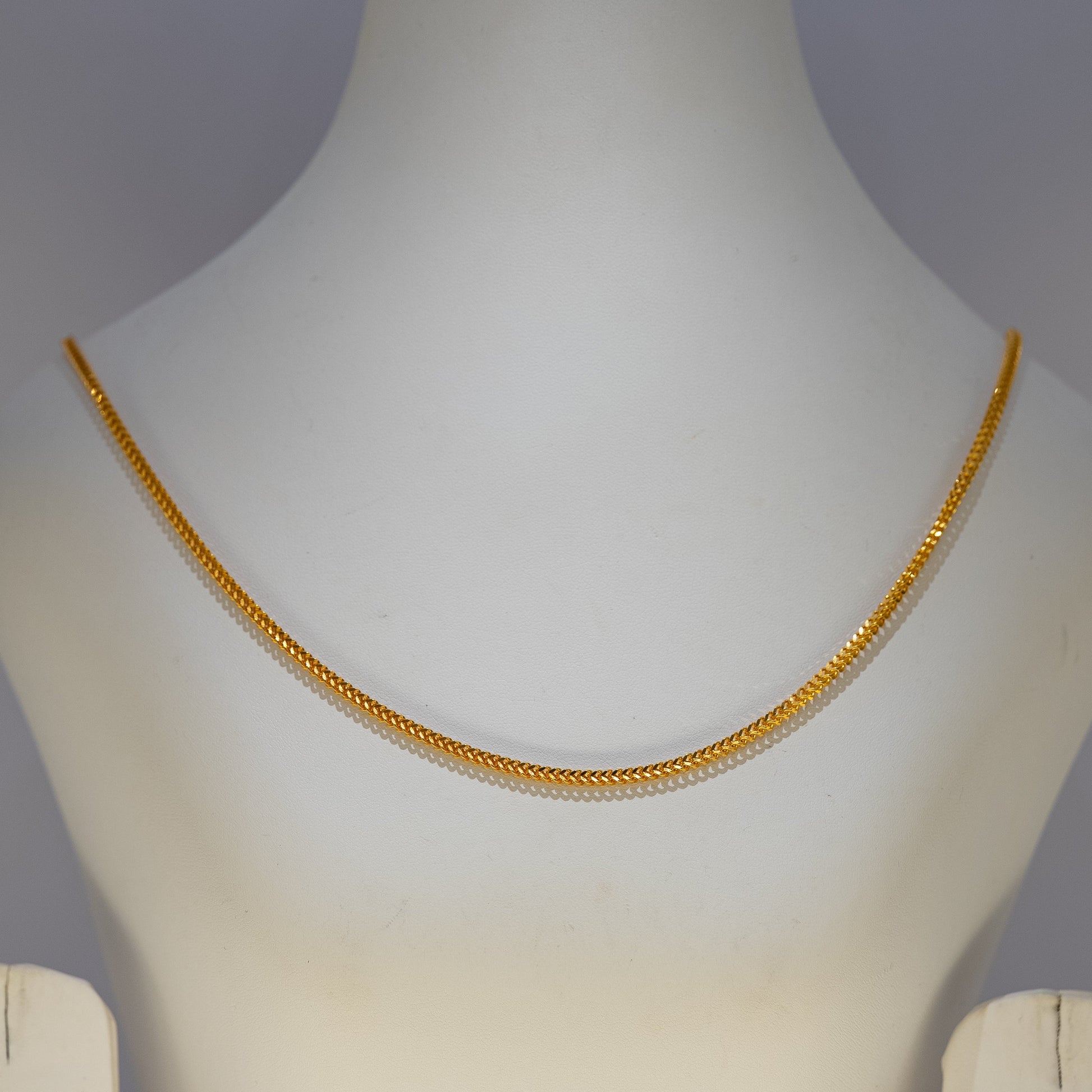 Gold necklace on a mannequin against a gray background