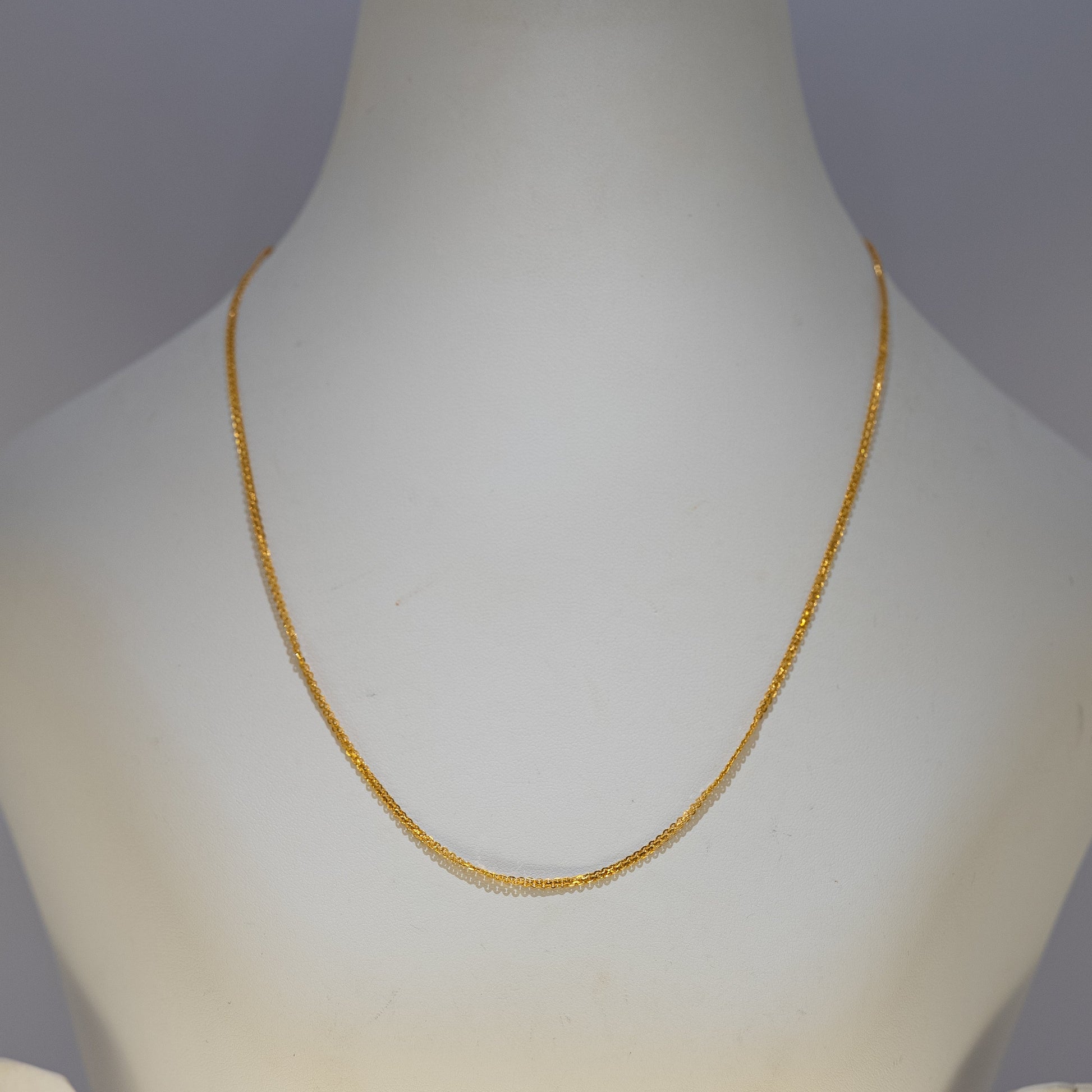 Gold necklace on a mannequin bust against a plain background