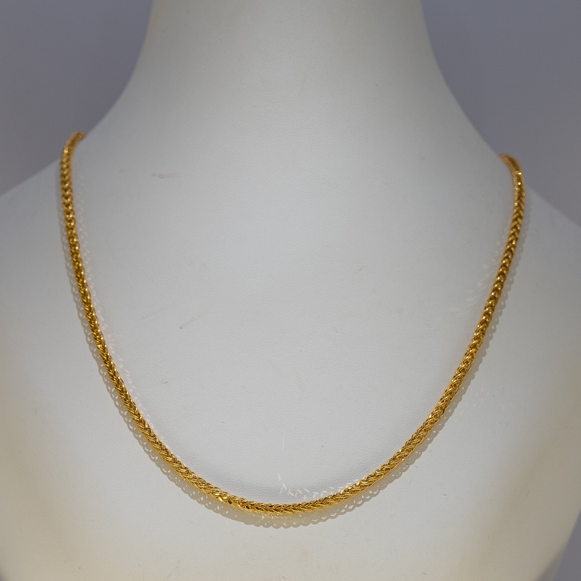 Gold necklace on a mannequin against a gray background