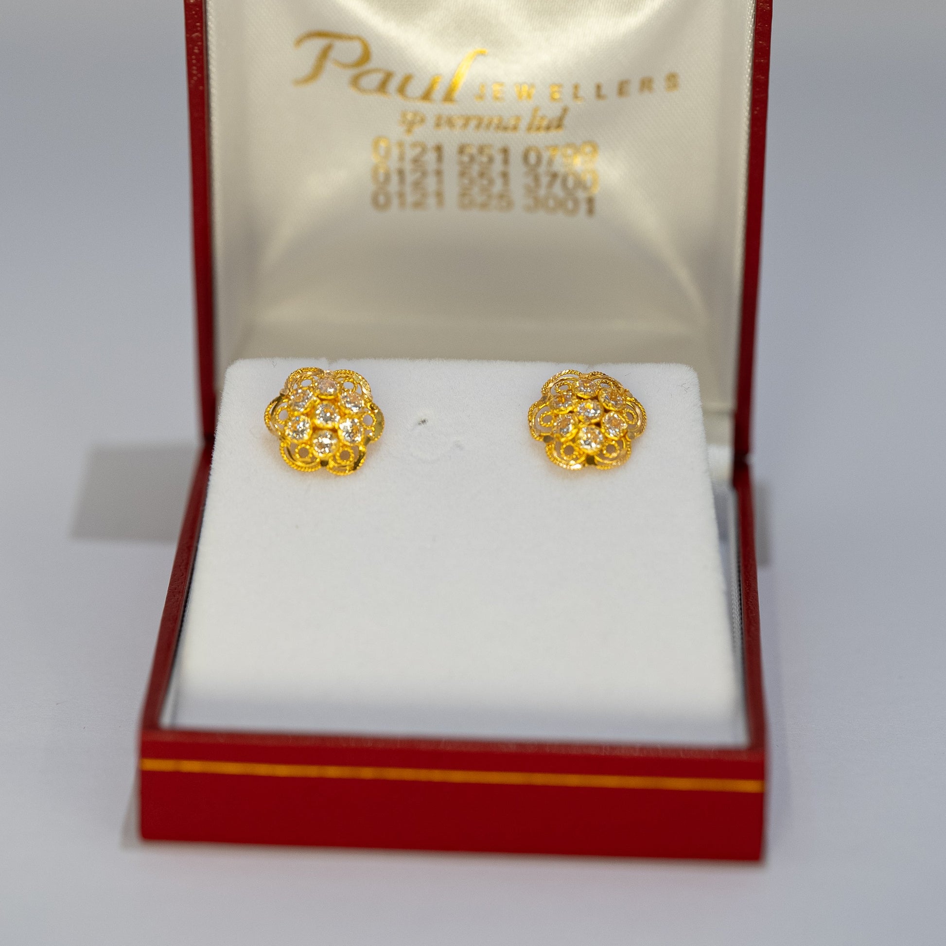 Gold earrings in a Paul's Jewels box on a gray background