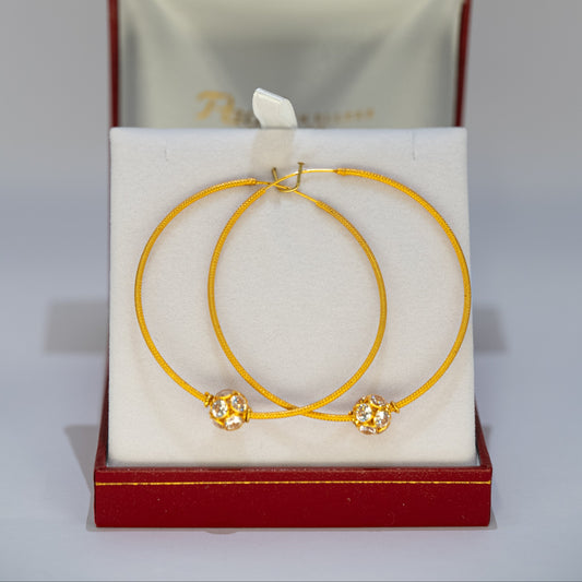 Gold hoop earrings with floral ends in a red jewelry box on a gray background