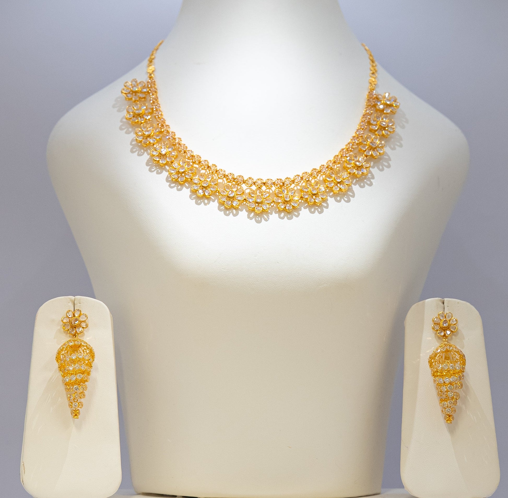 Gold necklace and earrings set on a mannequin bust with a plain background