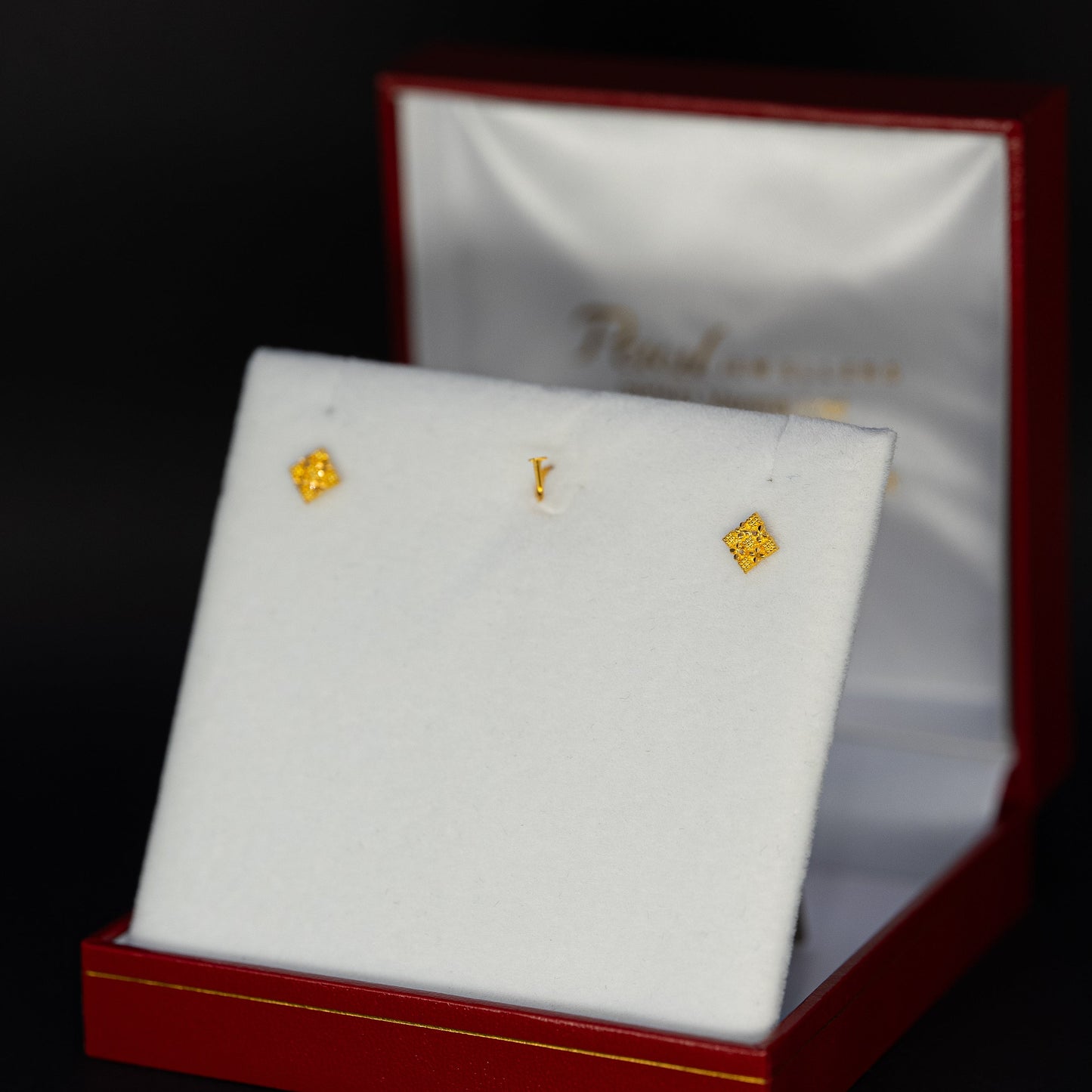 Gold earrings on a white display card in a red box with branding.