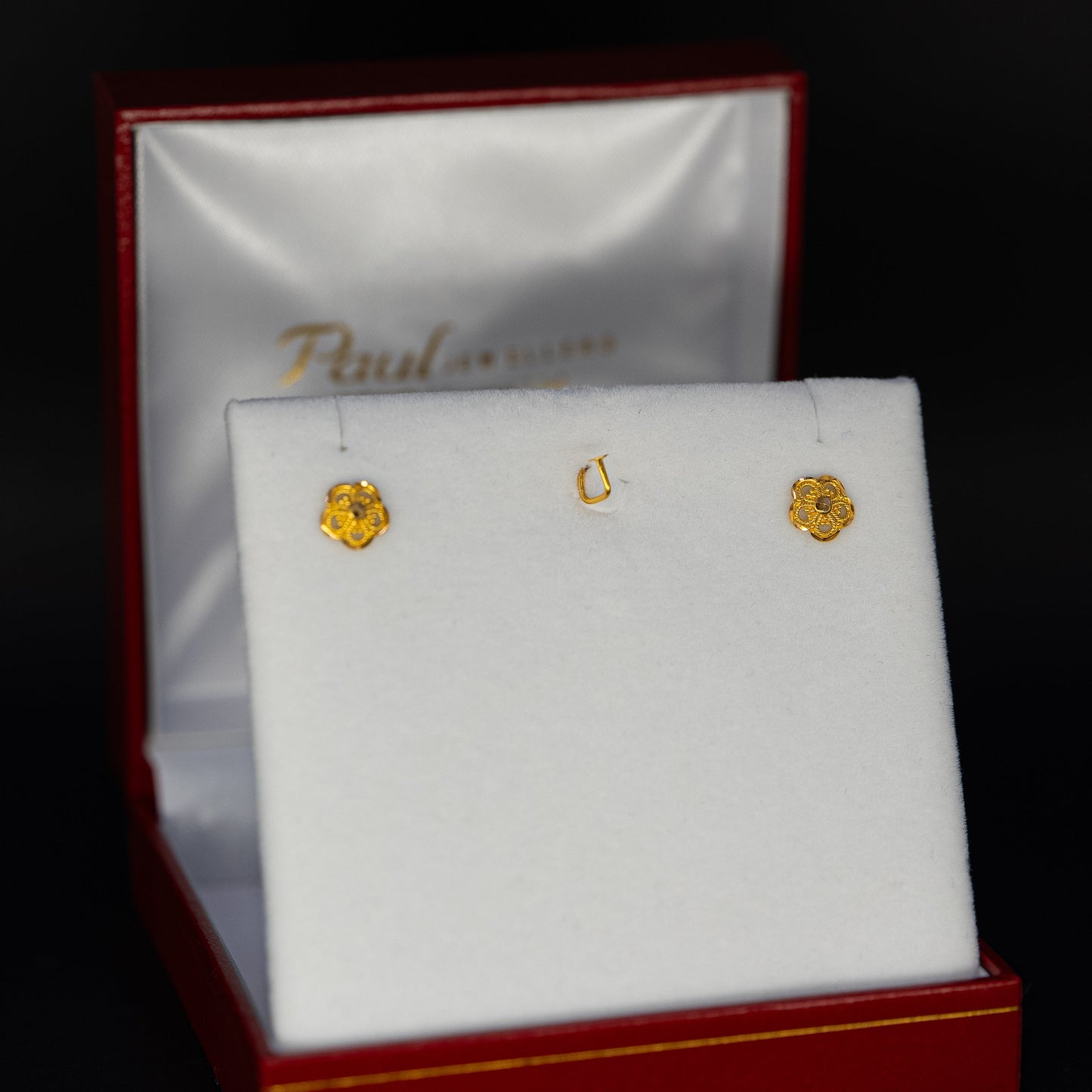 Gold earrings in a Paul jewelry box on a black background