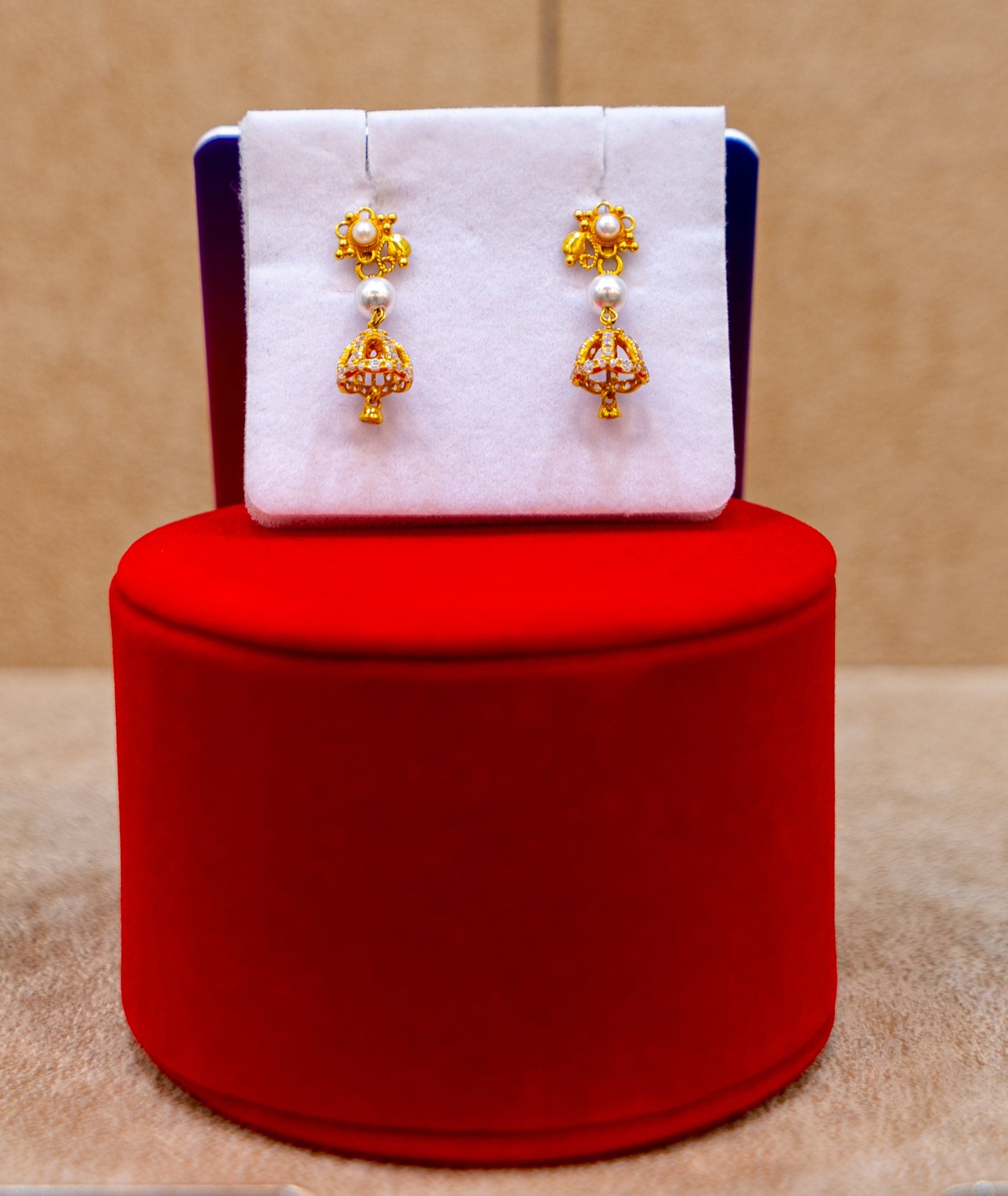 Gold earrings on a white card with a red cushion against a beige background