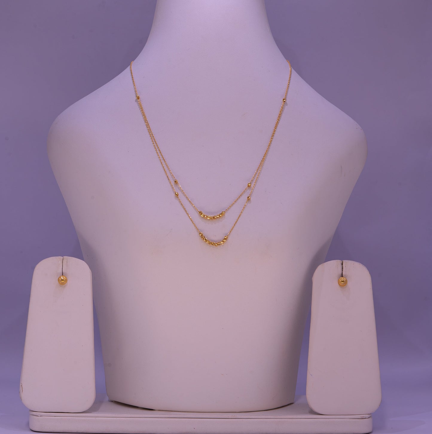 Gold necklace and earrings on a mannequin bust with a purple background