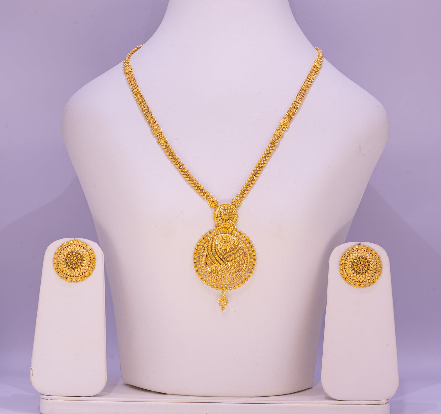 Gold necklace and earrings set on a white mannequin bust with a purple background