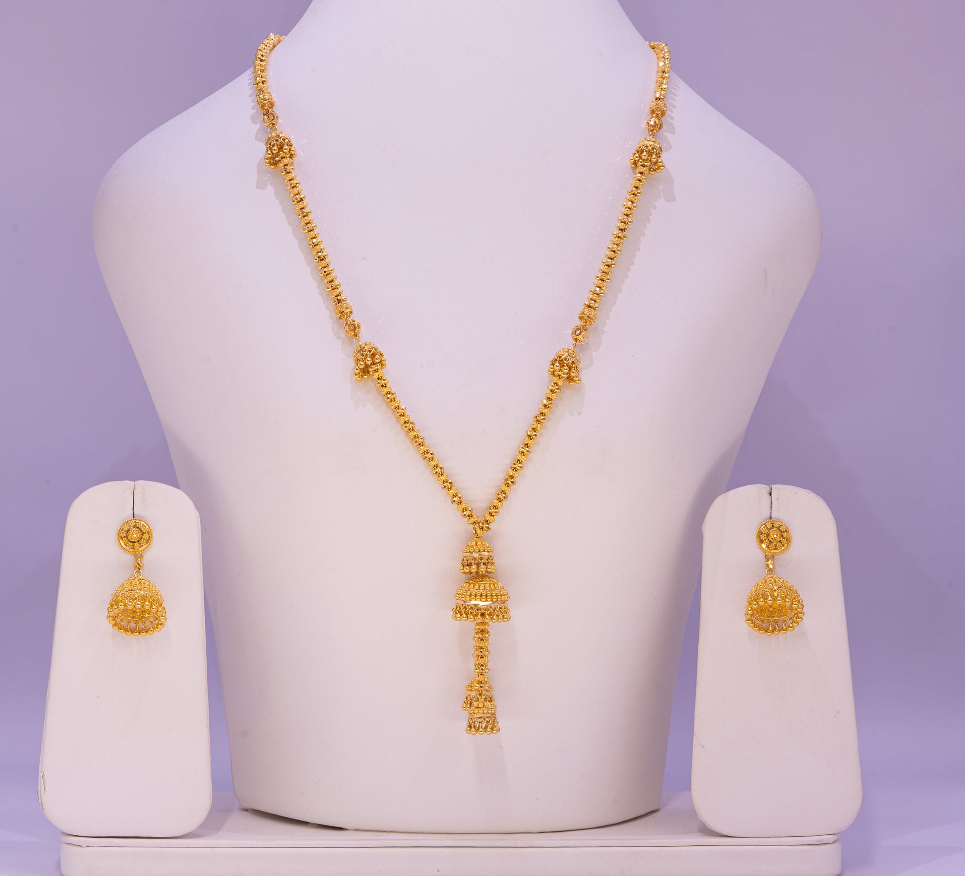 Gold necklace and earrings set on a mannequin bust with a purple background