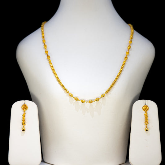 Gold necklace and earrings set on a mannequin bust against a black background