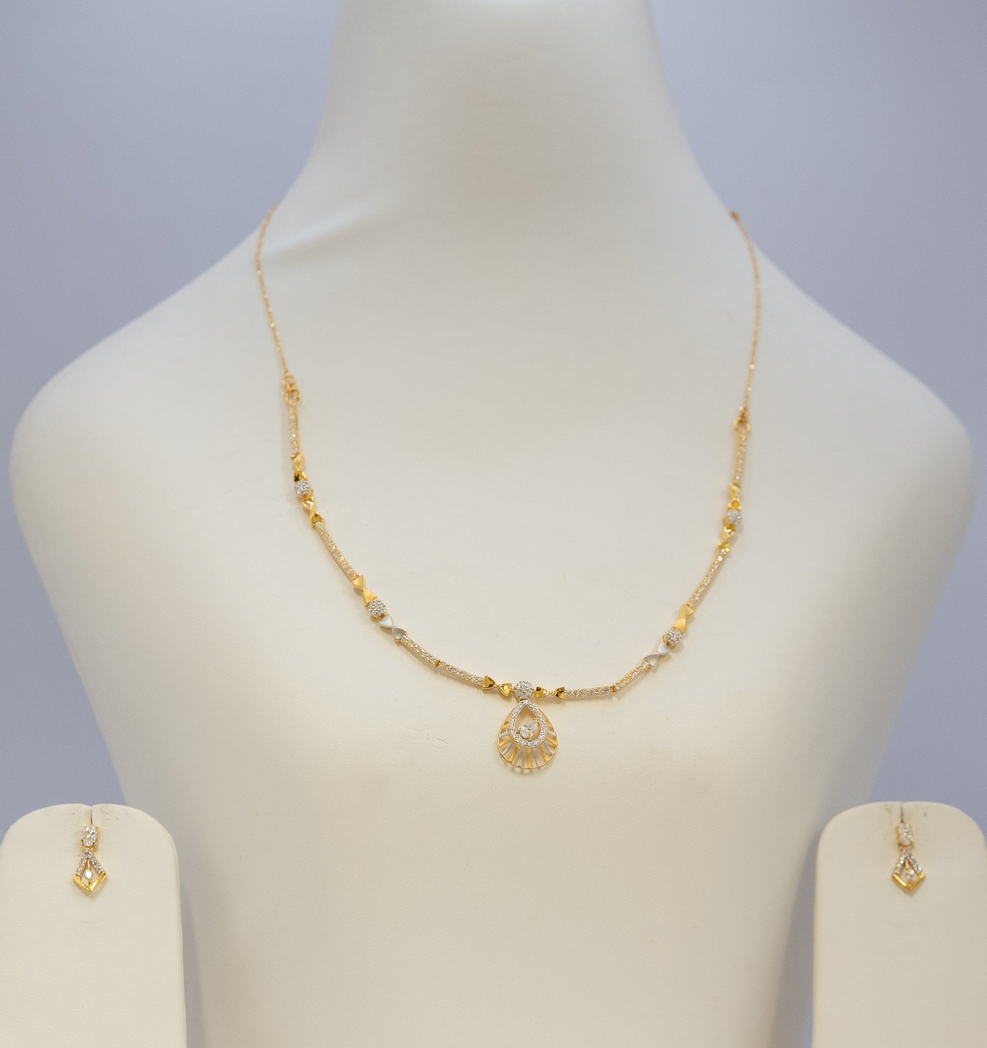 Gold necklace and earrings on a mannequin bust with a plain background