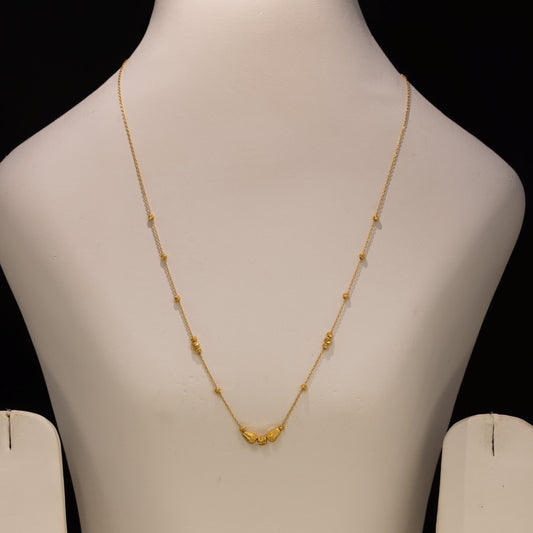 A delicate gold necklace with a small central cluster of beads, displayed on a white jewelry bust against a black background.