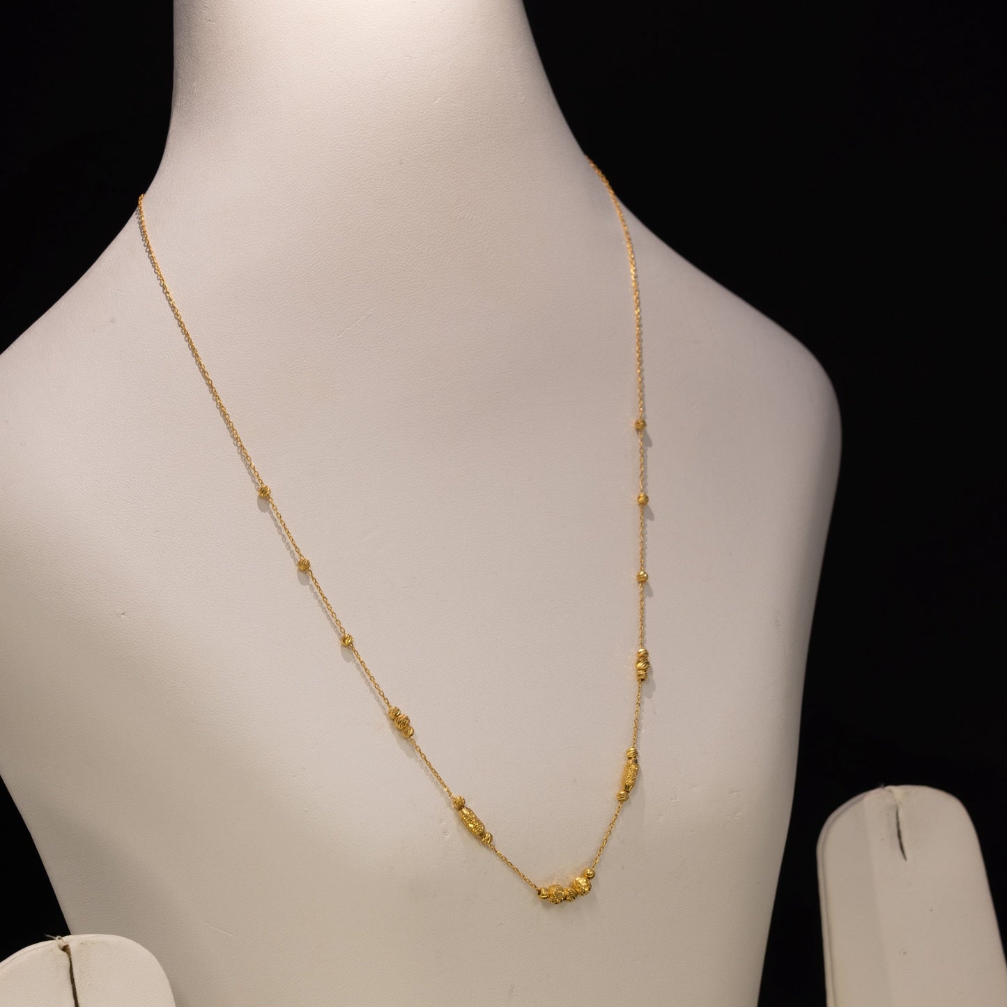 A delicate gold necklace displayed on a white jewelry bust against a black background.