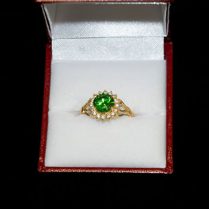 Gold ring with a green gemstone in an open jewelry box on a black background