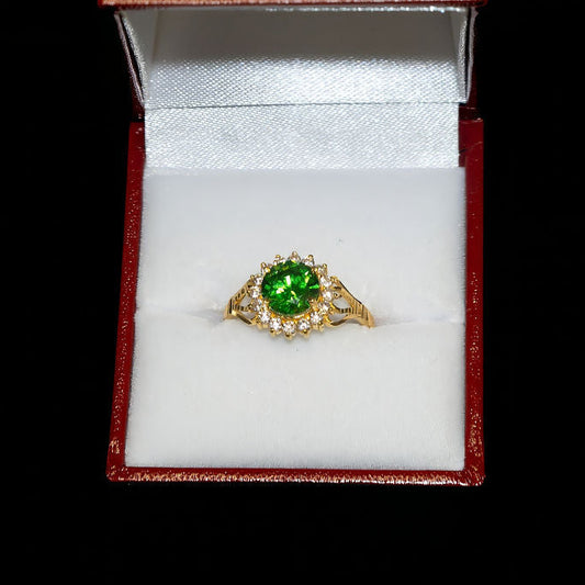 Gold ring with a green gemstone in an open jewelry box on a black background