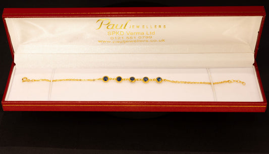 A gold chain bracelet with four dark green oval gemstones, presented in an open red Paul jewelry box on a black background.