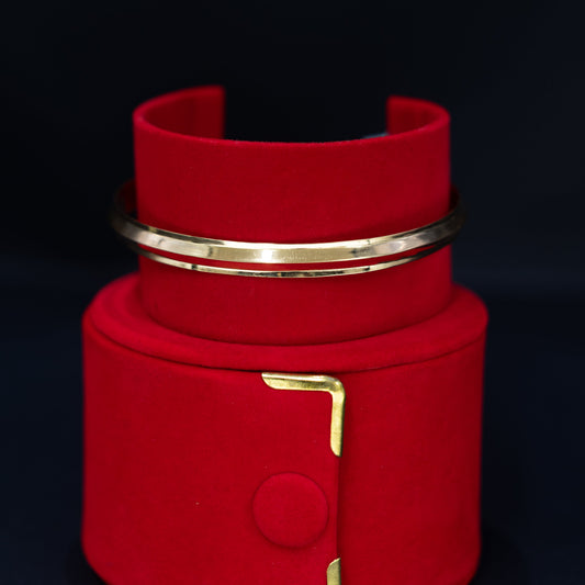 A red velvet jewelry display stand with gold-tone metal accents, holding a matching red cuff bracelet and a slim gold bangle, set against a dark background.