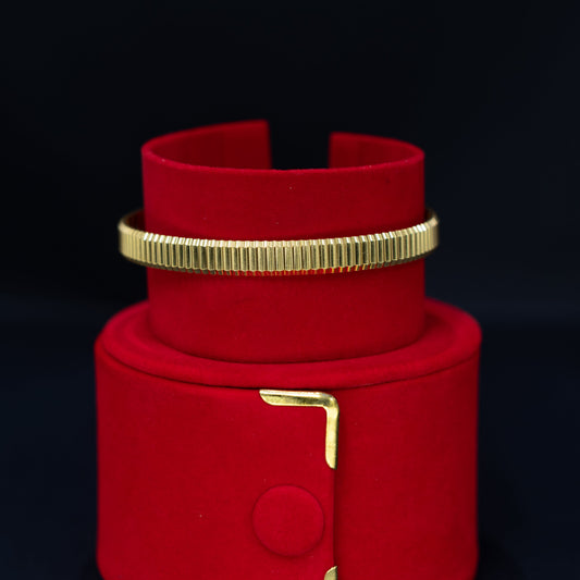 A red velvet jewelry display stand with gold-tone metal accents, holding a matching red cuff bracelet with a ribbed gold band.