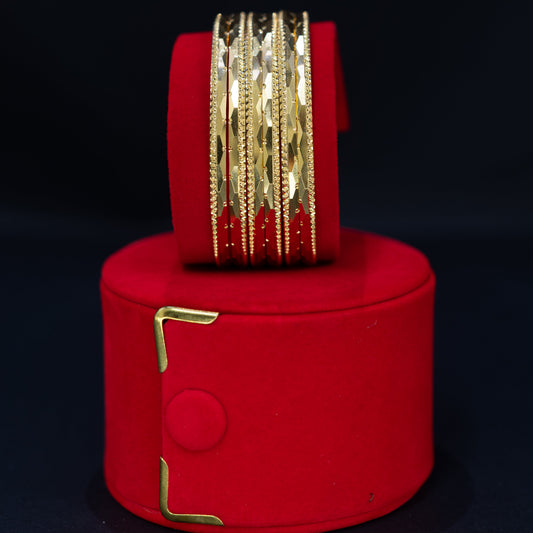 A set of gold-toned bangles displayed on a red cylindrical stand against a dark background.